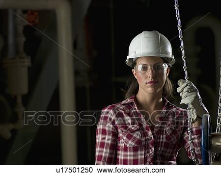 Stock Image - Woman wearing hard hat in industrial setting. Fotosearch