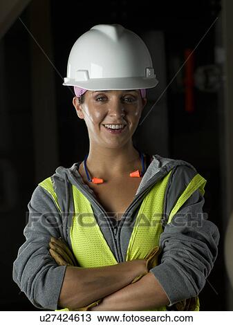 Stock Image - Woman wearing hard hat in industrial setting. Fotosearch