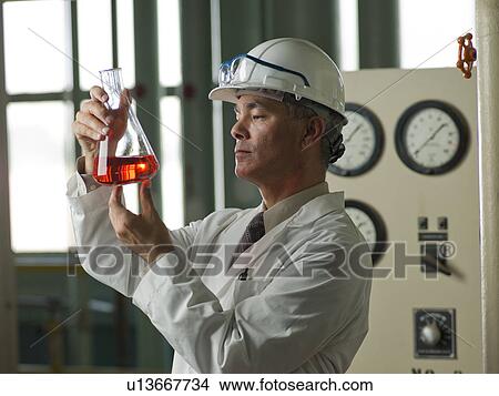 Worker in lab coat examining liquid in beaker View Large Photo Image Picture - Worker in lab coat examining liquid in beaker. Fotosearch