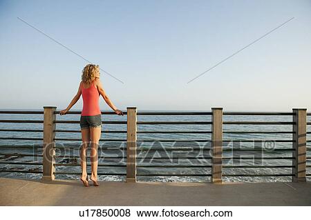 Stock Photo - Young attractive woman contemplating seascape from terrace. Fotosearch