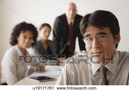 Stock Image - Young businessman looking at camera, business team in background. Fotosearch