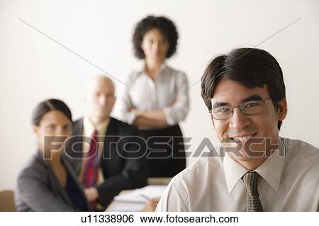 Young businessman looking at camera, business team in background View Large Photo Image Stock Photograph - Young businessman looking at camera, business team in background. Fotosearch