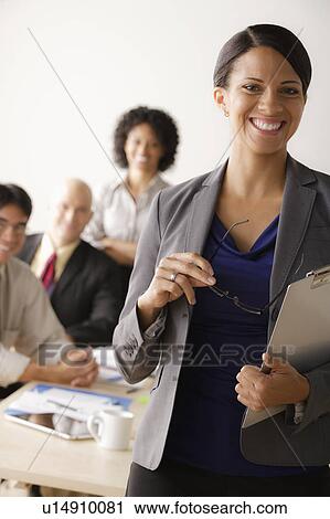 Stock Image - Young businesswoman looking at camera, business team in background. Fotosearch