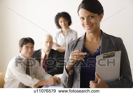 Stock Photo - Young businesswoman looking at camera, business team in background. Fotosearch