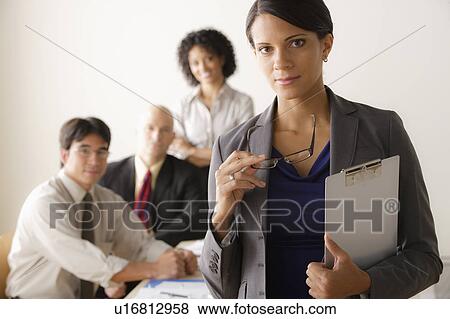 Stock Photo - Young businesswoman looking at camera, business team in background. Fotosearch