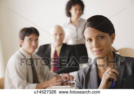 Stock Photograph - Young businesswoman looking at camera, business team in background. Fotosearch
