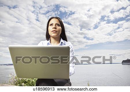 Young businesswoman using laptop on lakeshore View Large Photo Image Stock Image - Young businesswoman using laptop on lakeshore. Fotosearch