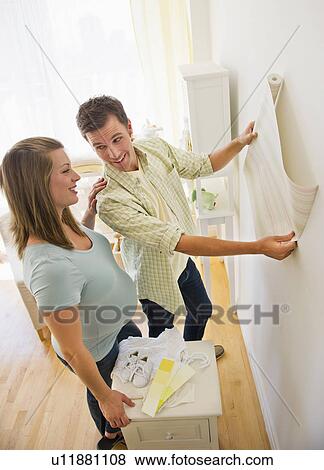 Stock Photo - Young couple choosing wallpaper for nursery. Fotosearch