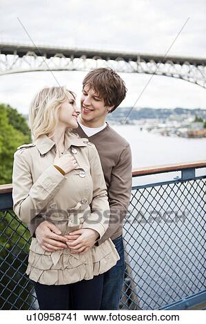 Young couple embracing on bridge View Large Photo Image Stock Image - Young couple embracing on bridge. Fotosearch