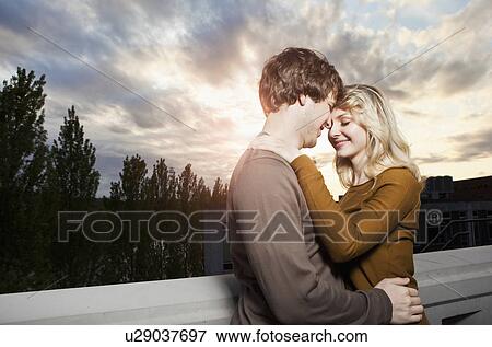 Young couple embracing under sunset sky View Large Photo Image Stock Photo - Young couple embracing under sunset sky. Fotosearch