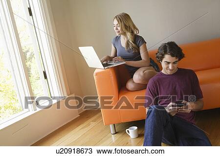 Young couple in living room, using phone and laptop View Large Photo Image Stock Image - Young couple in living room, using phone and laptop. Fotosearch