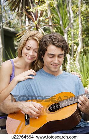 Picture - Young couple in park, man playing guitar. Fotosearch