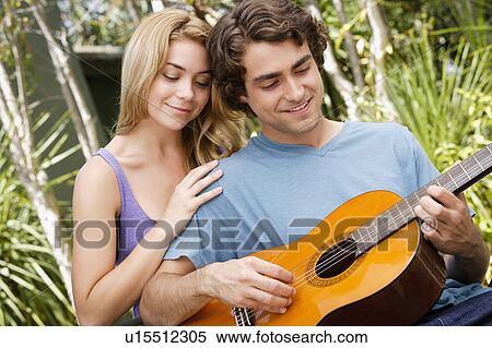 Stock Photography - Young couple in park, man playing guitar. Fotosearch