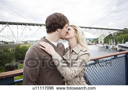 Young couple kissing on bridge View Large Photo Image Stock Photograph - Young couple kissing on bridge. Fotosearch