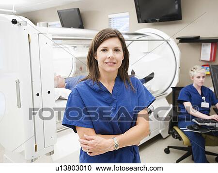 Stock Image - Young female nurse standing in front of CAT scanner. Fotosearch