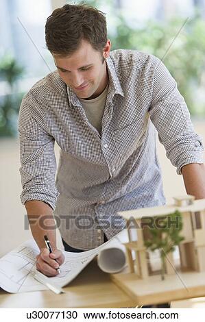 Stock Image - Young man doing notes at blueprints. Fotosearch