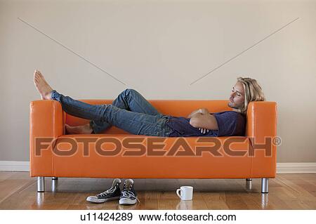 Young man lying on sofa View Large Photo Image Stock Photo - Young man lying on sofa. Fotosearch
