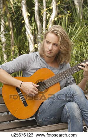 Young man playing guitar in park View Large Photo Image Stock Image - Young man playing guitar in park. Fotosearch