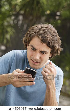 Stock Photo - Young man text-messaging and shaking fist. Fotosearch