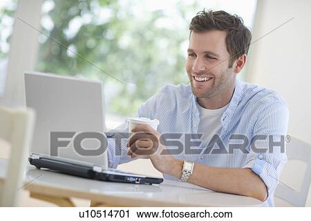 Stock Image - Young man using laptop and drinking coffee. Fotosearch
