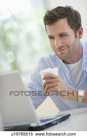 Stock Photography - Young man using laptop and drinking coffee. Fotosearch