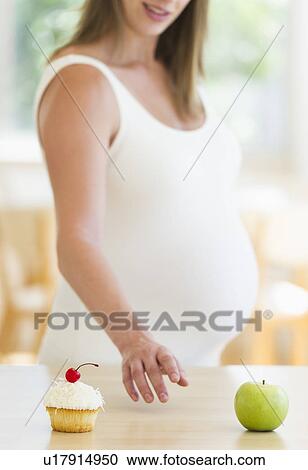 Young pregnant choosing between cupcake and apple View Large Photo Image Stock Image - Young pregnant choosing between cupcake and apple. Fotosearch