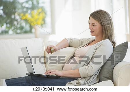 Stock Image - Young pregnant woman doing online shopping. Fotosearch