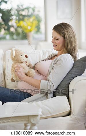 Stock Photo - Young pregnant woman on sofa with teddy bear. Fotosearch