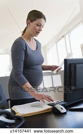 Stock Image - Young pregnant woman working in office. Fotosearch