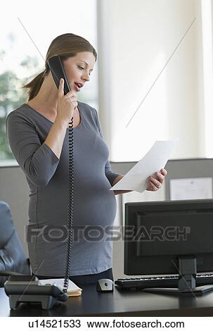 Stock Image - Young pregnant woman working in office. Fotosearch