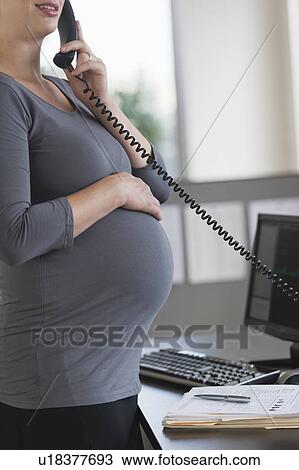 Stock Image - Young pregnant woman working in office. Fotosearch