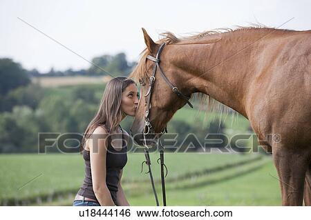 Stock Photograph - Young woman kissing horse in field. Fotosearch