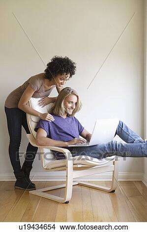 Young woman looking at man using laptop at home View Large Photo Image Picture - Young woman looking at man using laptop at home. Fotosearch