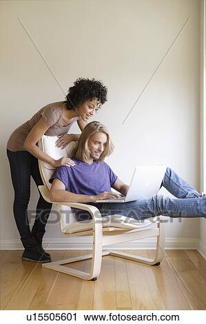 Young woman looking at man using laptop at home View Large Photo Image Stock Image - Young woman looking at man using laptop at home. Fotosearch