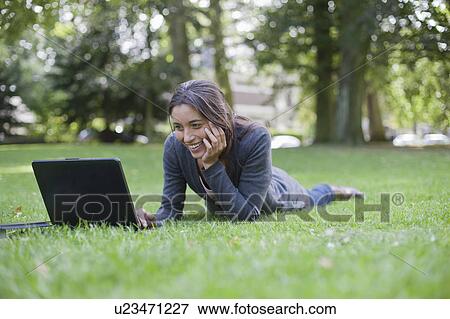 Young woman lying on grass using laptop View Large Photo Image Stock Photo - Young woman lying on grass using laptop. Fotosearch