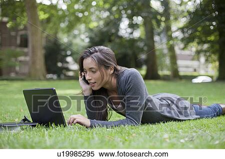 Young woman lying on grass using laptop and cell phone View Large Photo Image Stock Photography - Young woman lying on grass using laptop and cell phone. Fotosearch