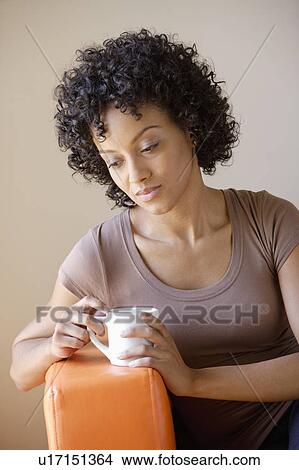 Picture - Young woman sitting in armchair holding cup. Fotosearch