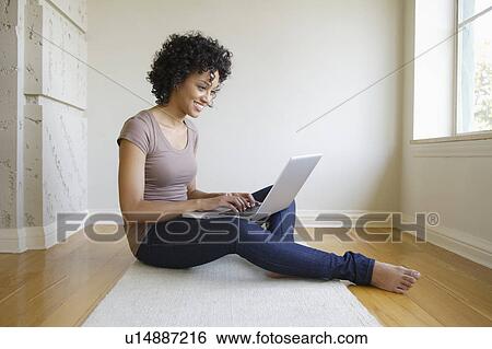 Young woman sitting in room using laptop View Large Photo Image Stock Photograph - Young woman sitting in room using laptop. Fotosearch