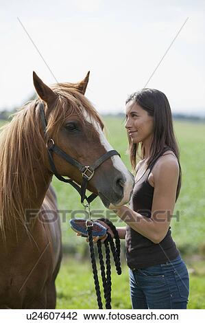 Stock Image - Young woman taking care of horse. Fotosearch