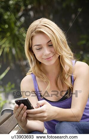 Stock Image - Young woman text-messaging in park. Fotosearch