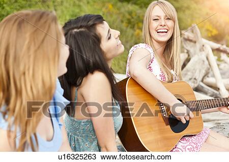 Stock Image - Young women playing guitar on beach. Fotosearch