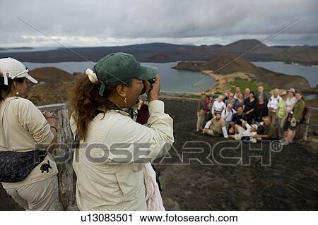 Stock Image - Female tourists taking picture of their friends from an extinct volcanic mountain, Bartolome island, Galapagos Islands, Ecuador. Fotosearch