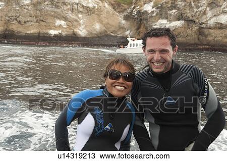 Stock Image - Happy couple smiling in wet suits, Kicker Rock, San Cristobal Island, Galapagos Islands, Ecuador. Fotosearch