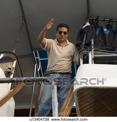 Low angle view of a man standing on a boat, Puerto Ayora, Santa Cruz Island, Galapagos Islands, Ecuador View Large Photo Image Stock Photo - Low angle view of a man standing on a boat, Puerto Ayora, Santa Cruz Island, Galapagos Islands, Ecuador. Fotosearch