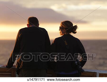 Stock Image - Rear view of a couple standing on the boat looking at a view, Galapagos Islands, Ecuador. Fotosearch