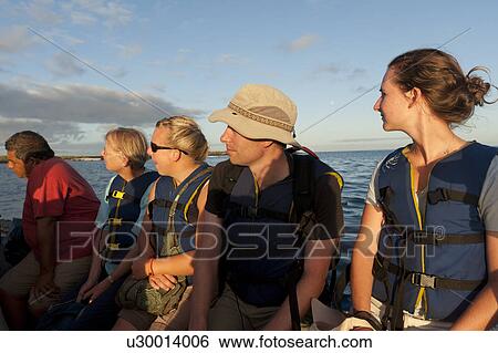 Stock Photograph - Tourists sitting on a boat, Punta Suarez, Espanola Island, Galapagos Islands, Ecuador. Fotosearch