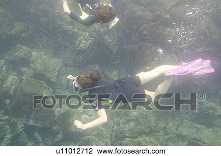 Stock Image - Two women swimming underwater, San Cristobal Island, Galapagos Islands, Ecuador. Fotosearch