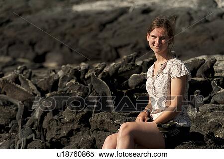 Stock Photography - Woman sitting on the beach near Marine iguanas (Amblyrhynchus cristatus), Punta Espinoza, Fernandina Island, Galapagos Islands, Ecuador. Fotosearch