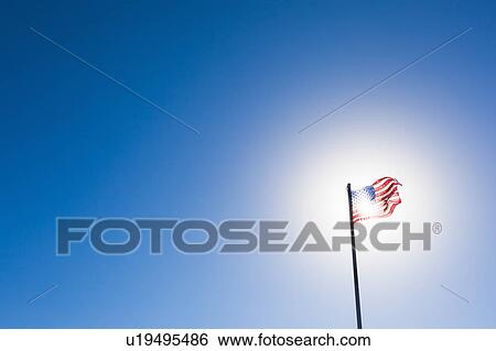 Stock Photograph - American flag against sun and blue sky. Fotosearch