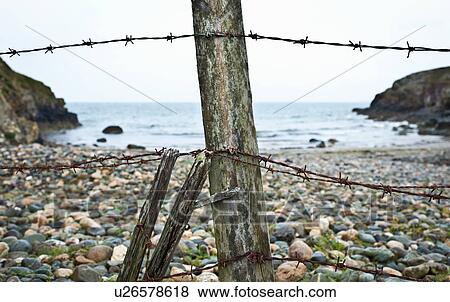Stock Photo - Barbed wire fence on rocky beach. Fotosearch